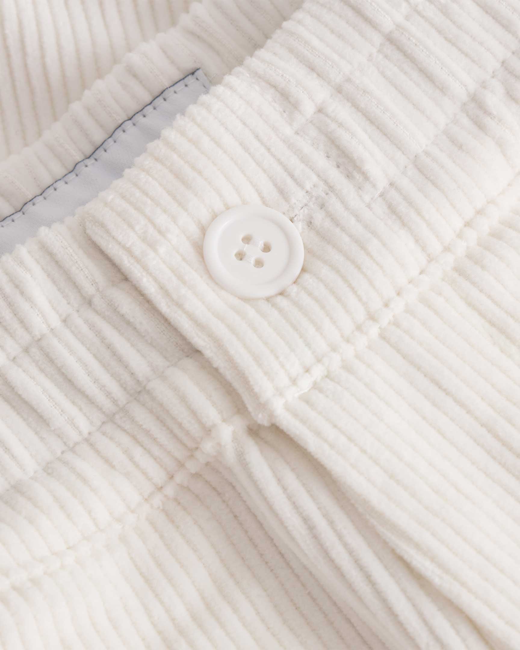 Close up of button closure on white and green corduroy track suit pants with NB embroidery