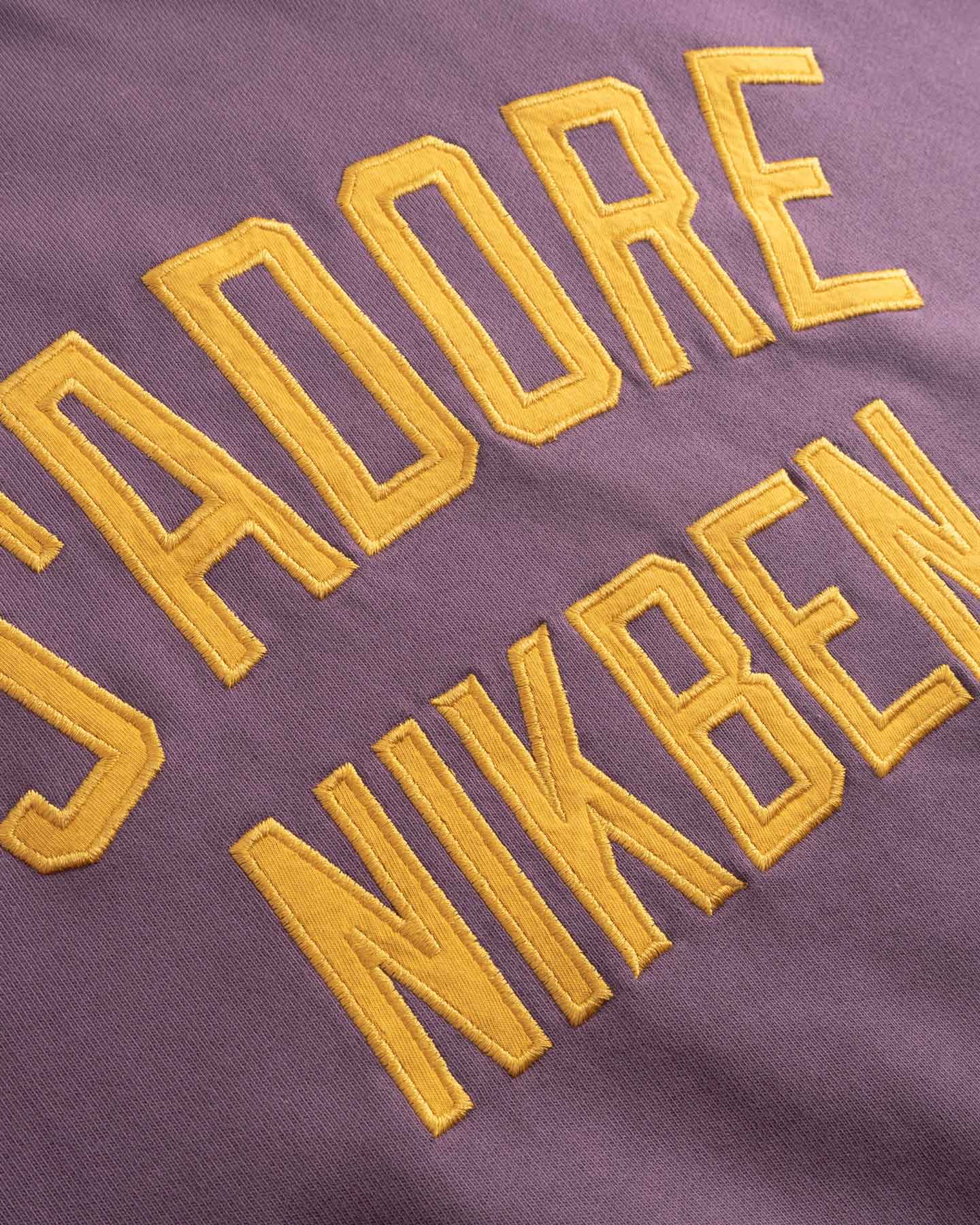 Yellow Text 'I adore NIKBEN' embroidered on a purple fabric.
