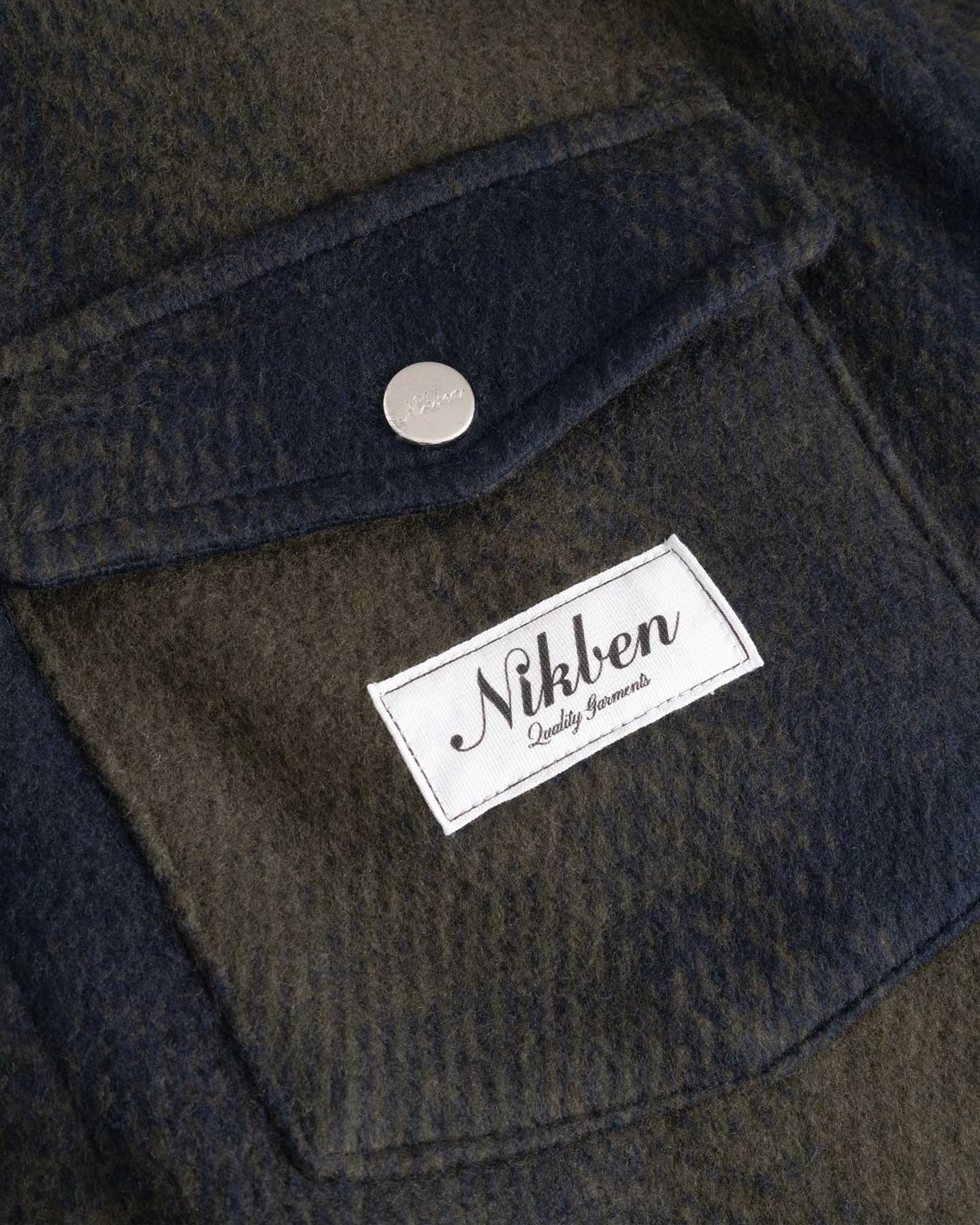 Close up on dark blue and green flannel overshirt front breast pocket with Nikben brand logo
