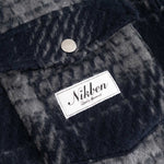 Close up of front chest pocket and logo on navy checkered shirt 
