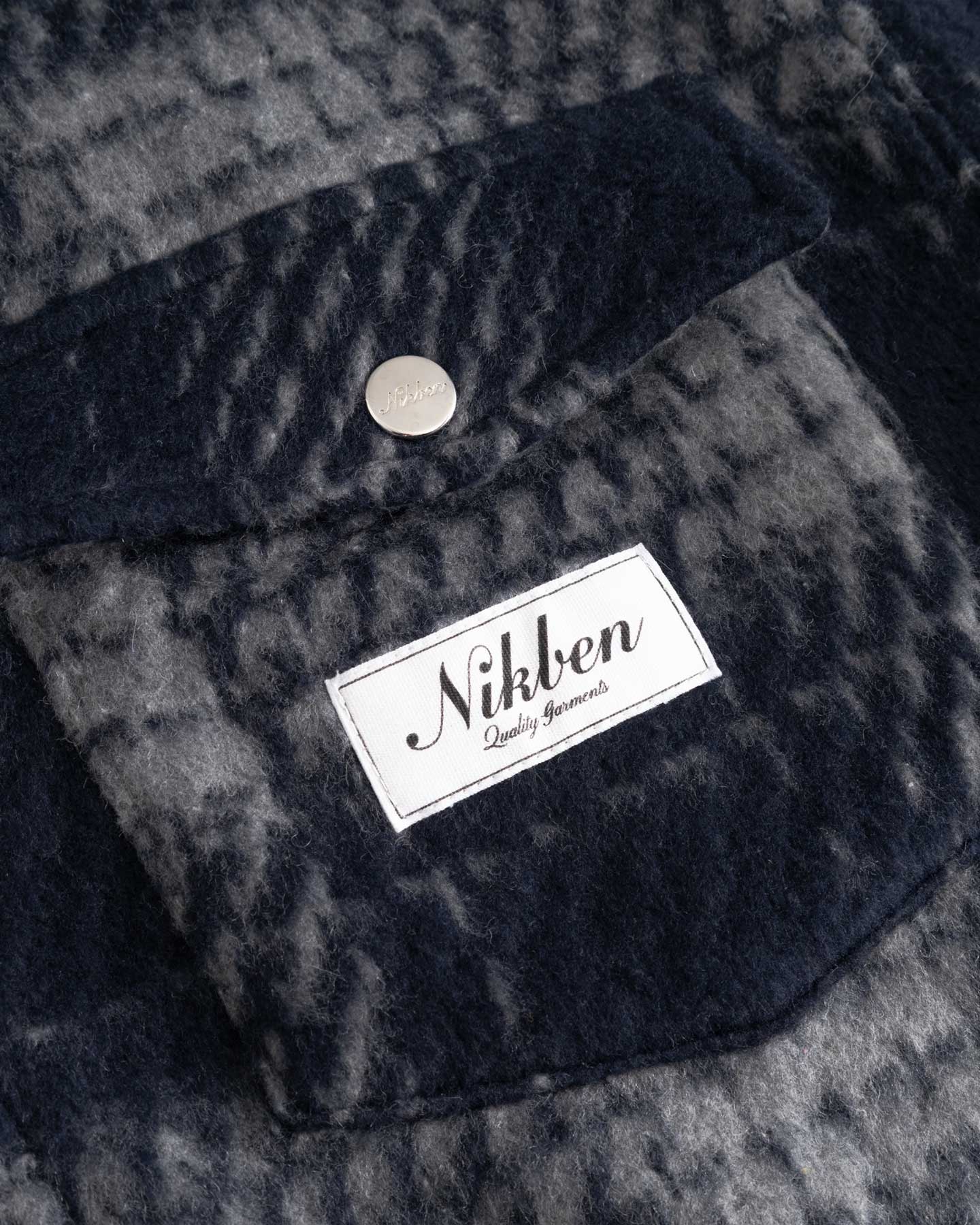 Close up of front chest pocket and logo on navy checkered shirt 
