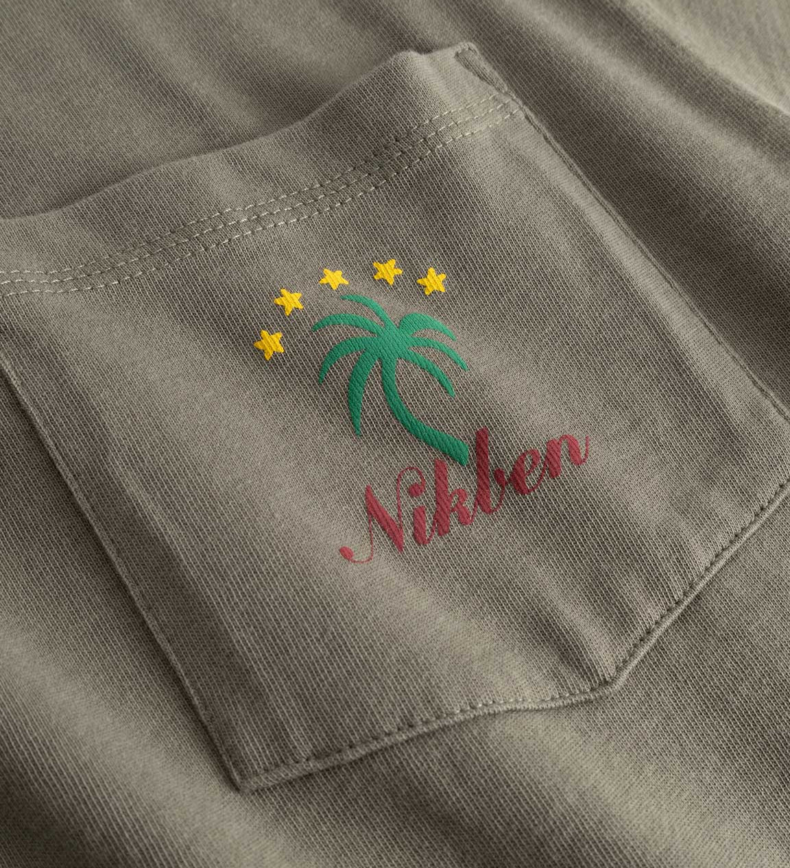 Closeup view of green palm print and red NIKBEN logo on front pocket of green T-shirt