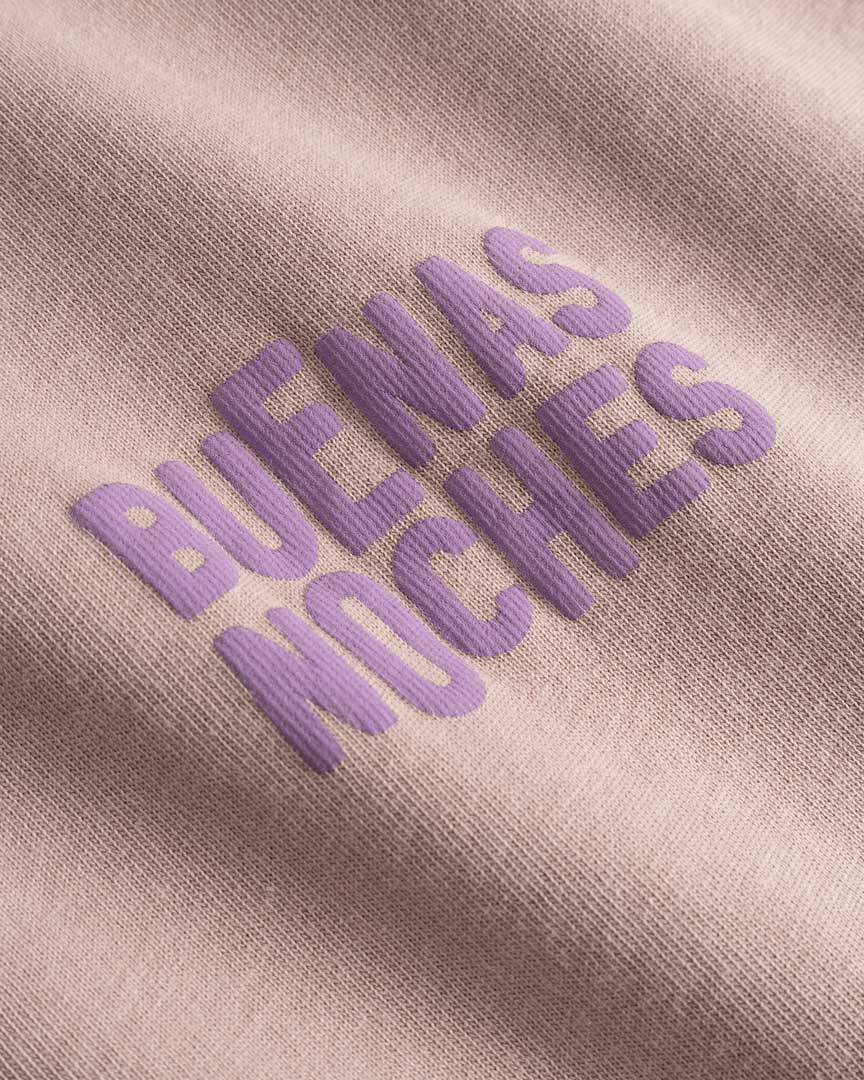 Closeup view of purple "BUENAS NOCHES" text print on brown T-shirt