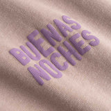 Closeup view of purple "BUENAS NOCHES" text print on brown T-shirt