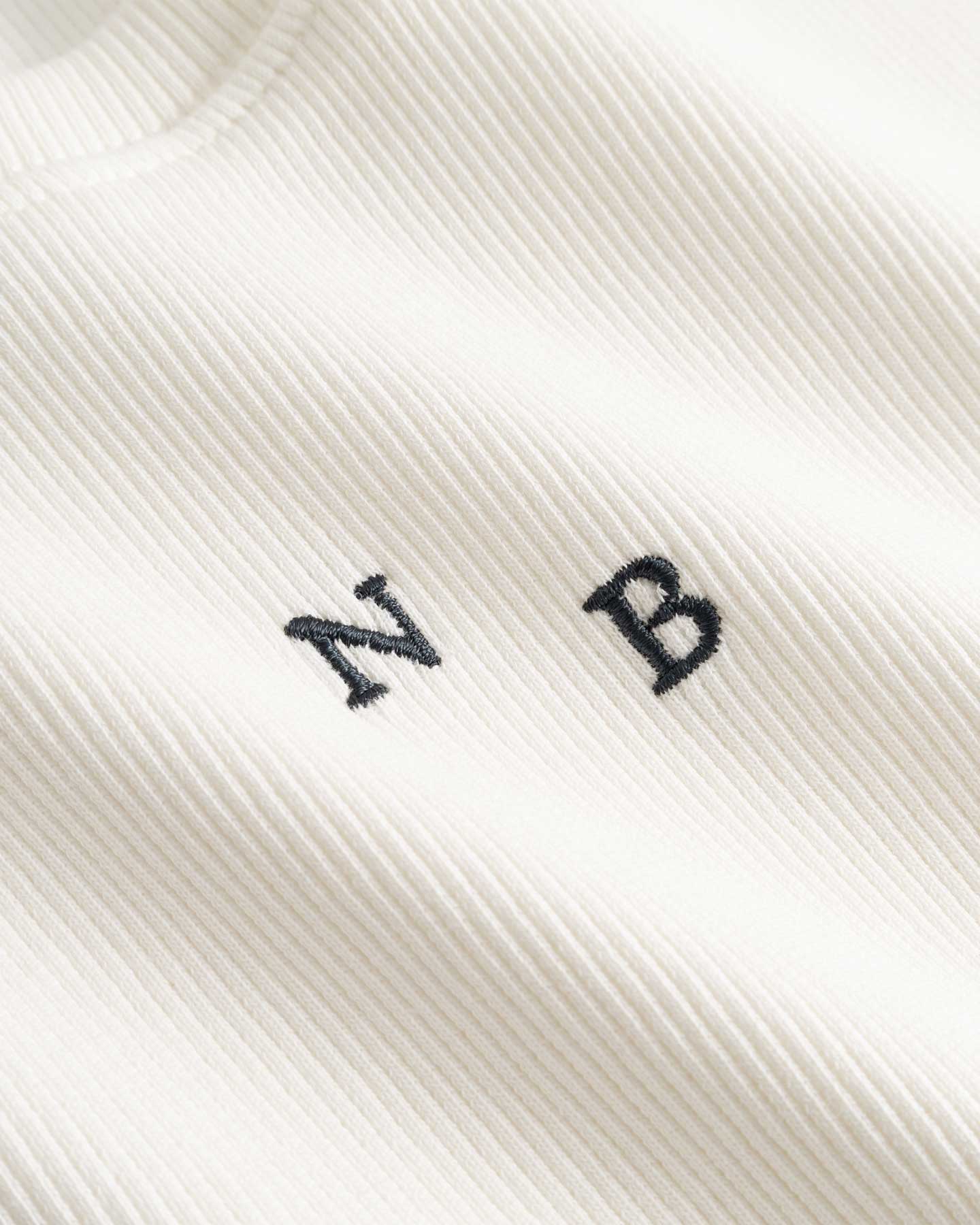 Closeup view of black NB initials on white ribbed tank top
