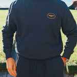Model wearing a complete black tracksuit with draw string and logo on front breast and lower leg