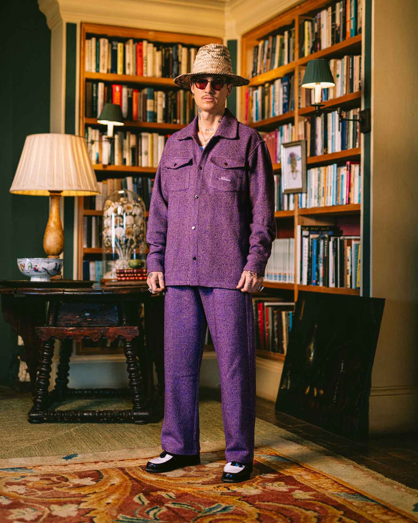 Model wearing a purple outfit standing in a room with bookshelves and decorative items.