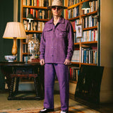 Model wearing a purple outfit standing in a room with bookshelves and decorative items.