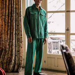 Model is wearing a green outfit standing in a room with a large window and patterned curtain.
