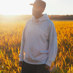 Model wearing a beige hoodie standing in a field with sunset light