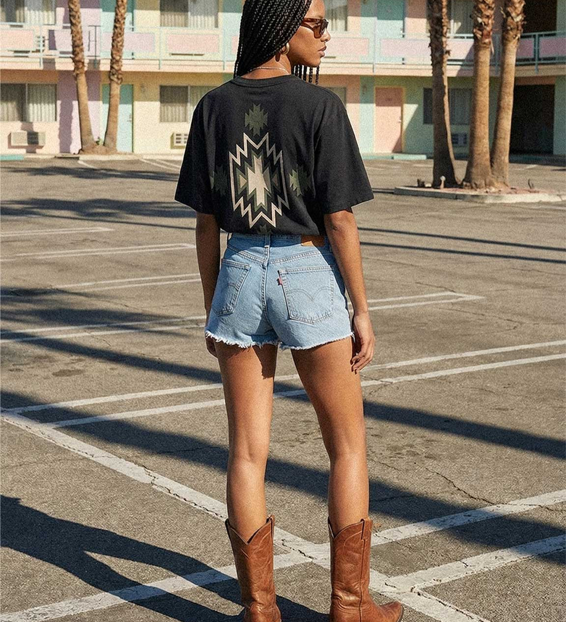 Back of female model wearing black T-shirt with native inspired backprint in green, white and black