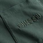Close up of chest pocket with tone in tone embroidered logo on washed green t-shirt.