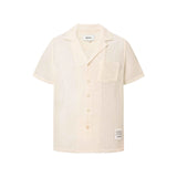 A short-sleeved off-white mesh shirt with pearl button closure and a front patch detail. The shirt is displayed in a flat lay format without a model.