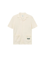 A short-sleeved, beige, waffle-patterned shirt with a collar, two pockets, and an embroidered logo on the pocket.