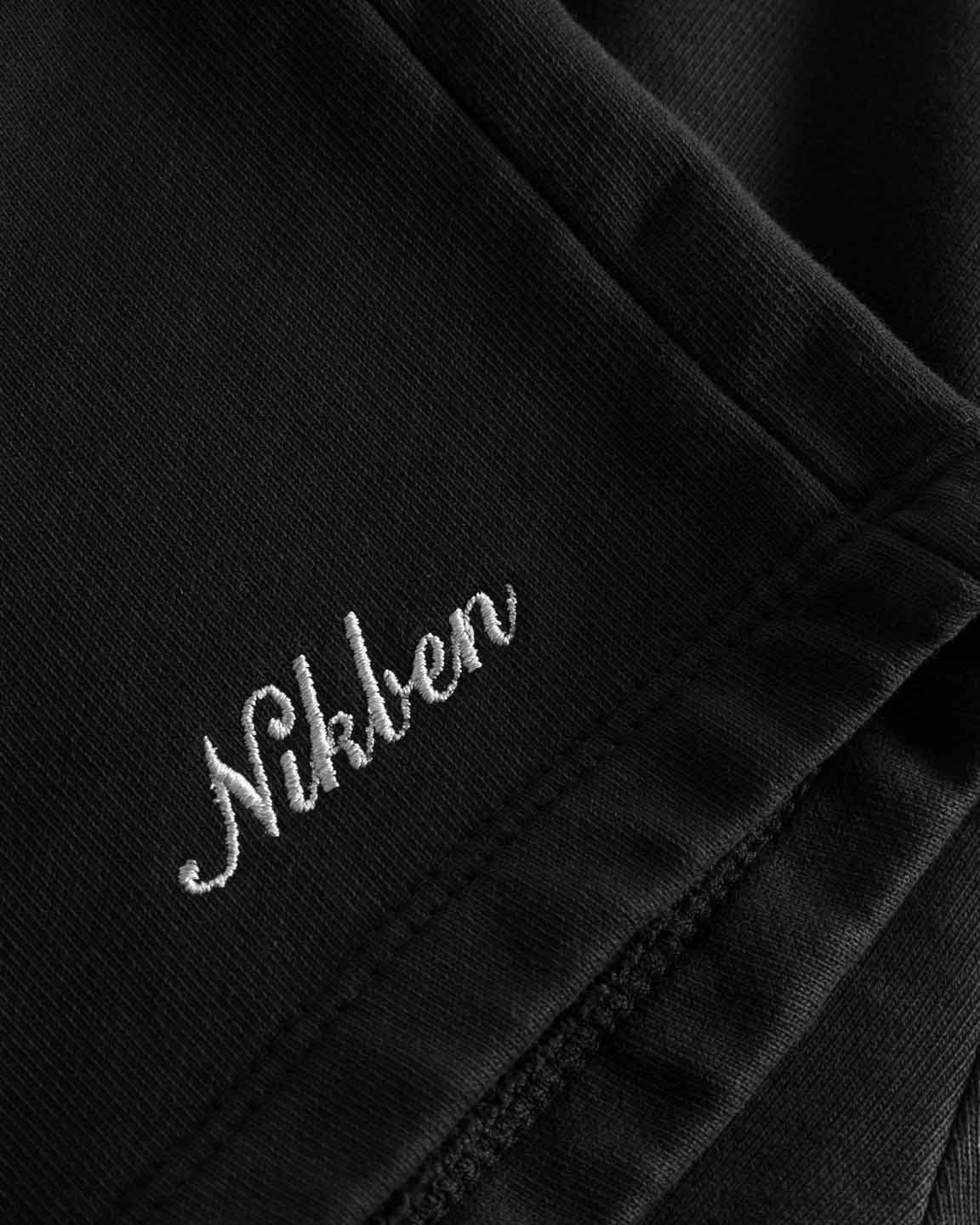 Close up on embroidered script logo on front leg of black washed sweatshorts