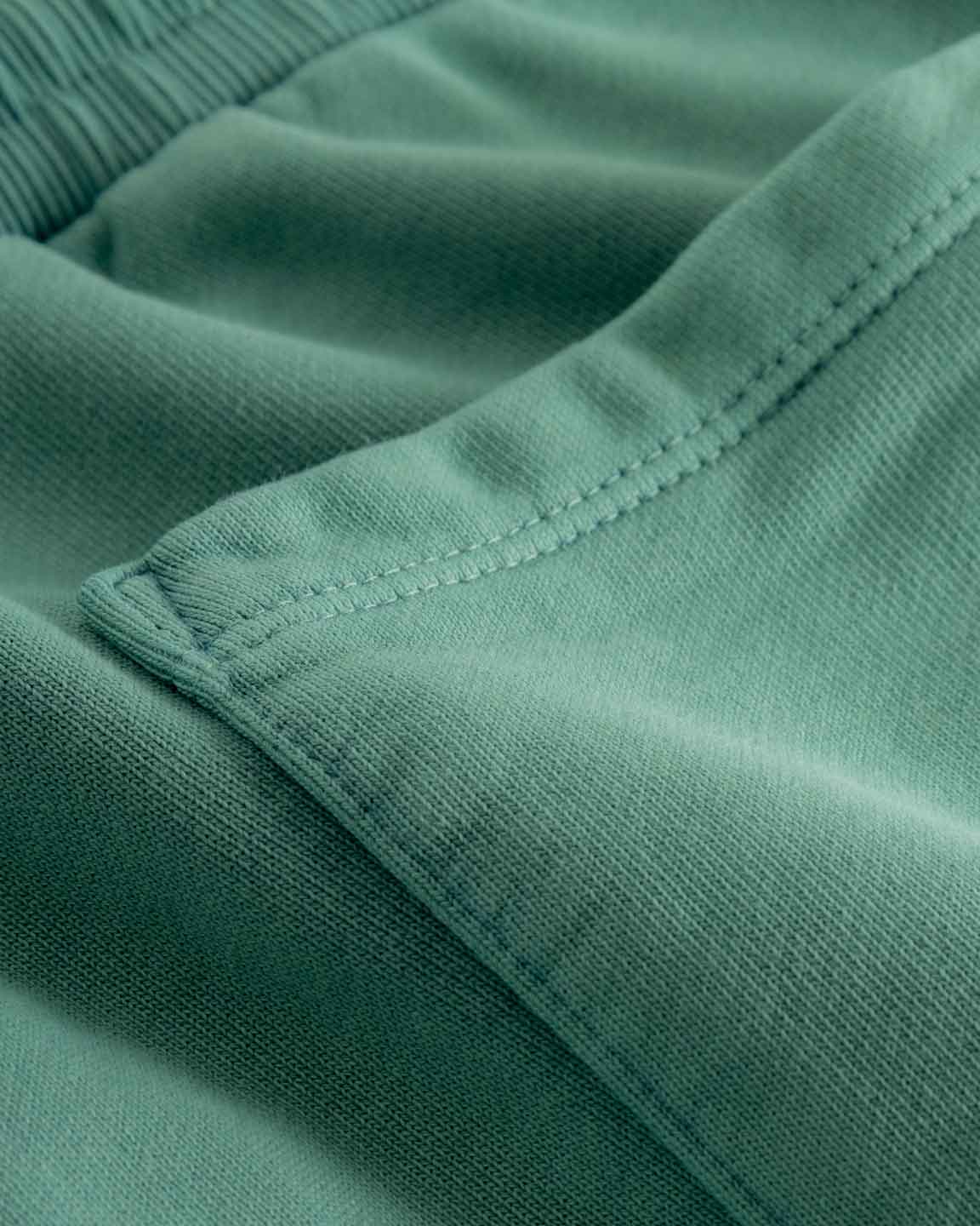Close up of back pocket and tonal stitchings on a pair of green sweatshorts