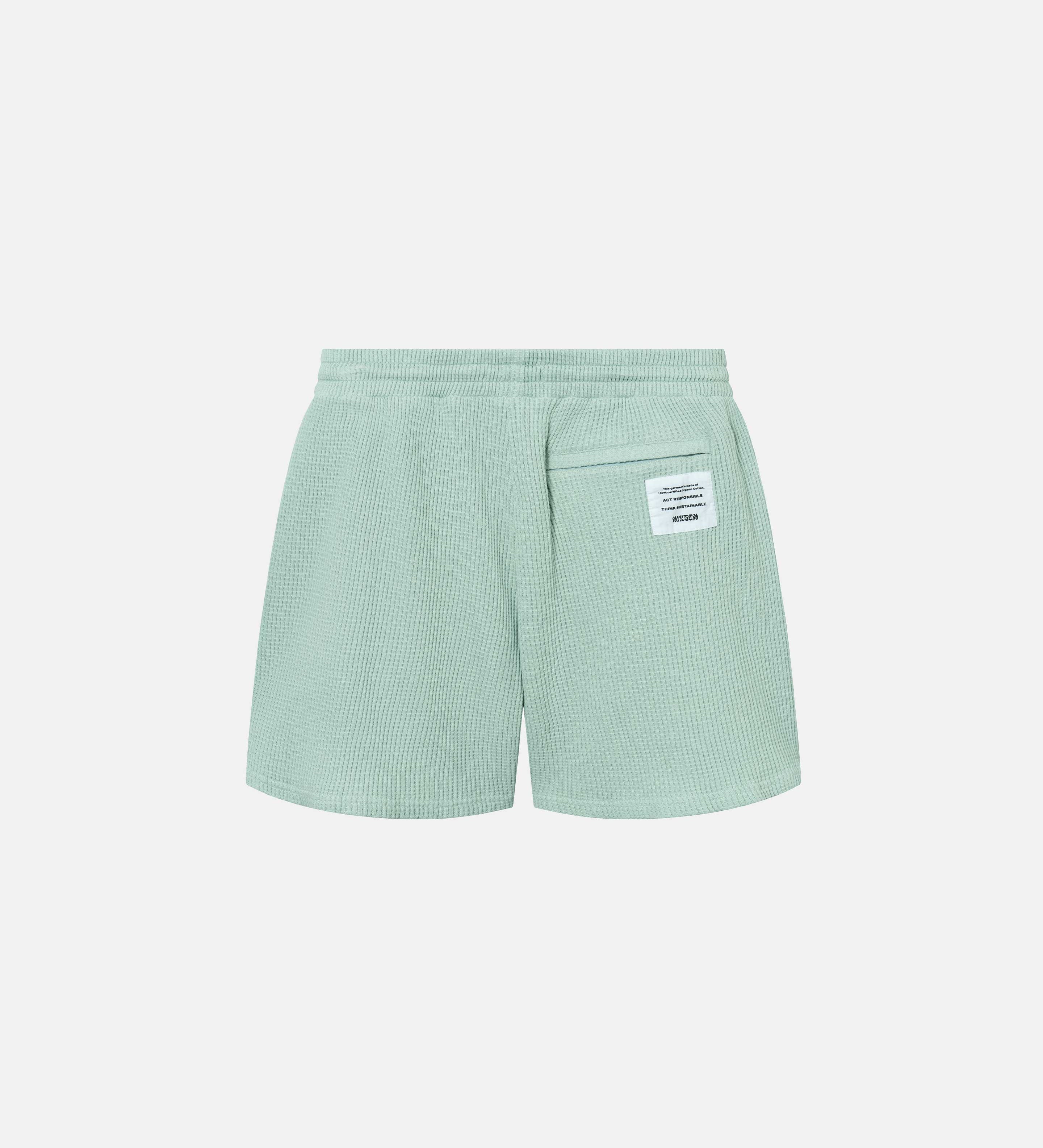 Backside of mint green waffle-patterned mid-length shorts with tone back pocket and logo patch.