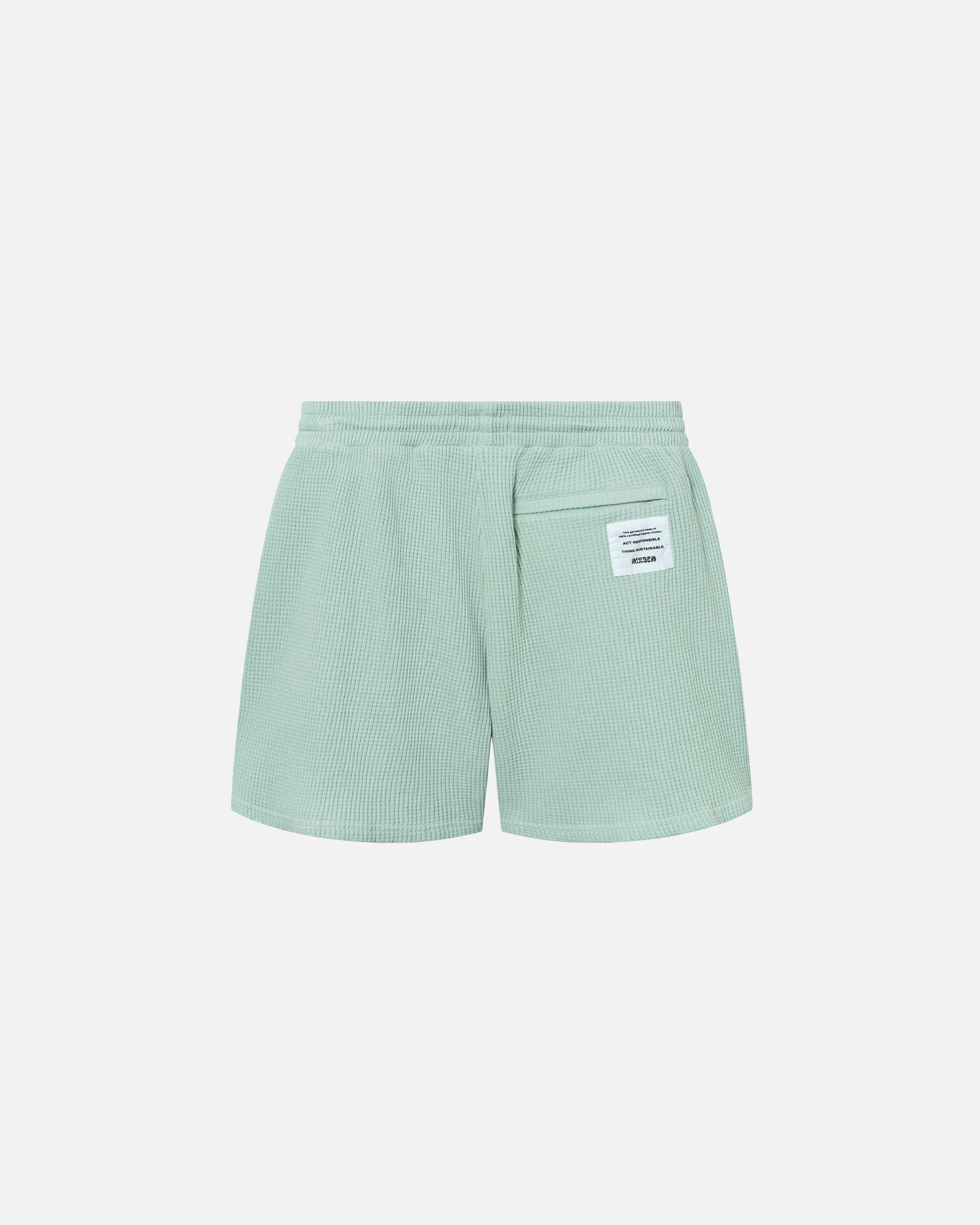 Backside of mint green waffle-patterned mid-length shorts with tone back pocket and logo patch.