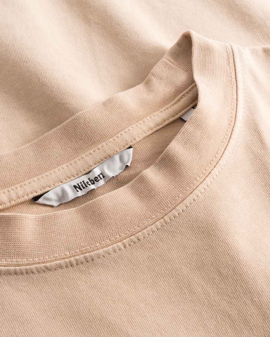 Close-up view of neck label, round neck, and tonal stitchings on a sand colored t-shirt