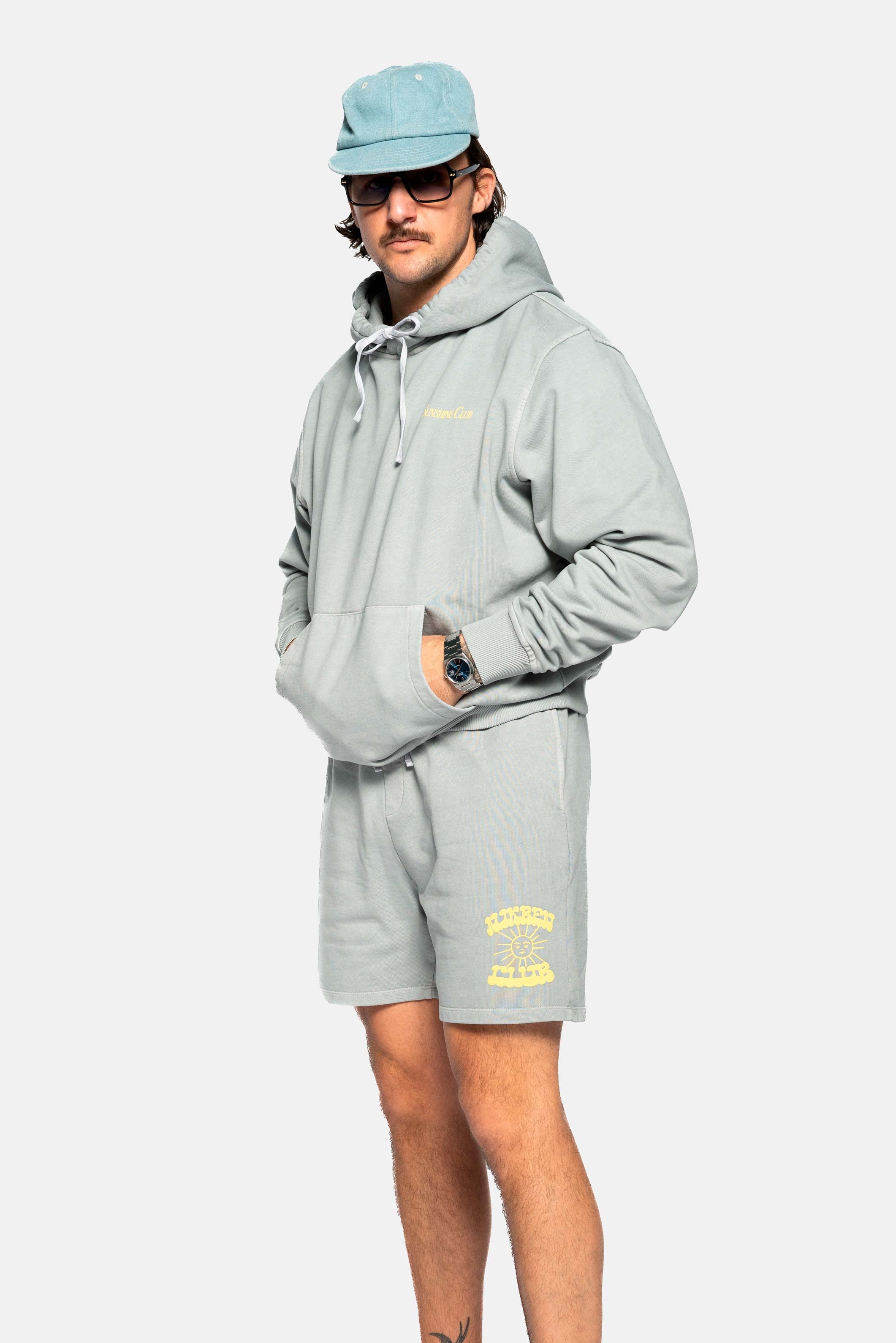 Male model wearing grey sweat shorts with drawstrings and yellow Nikben Sunshine Club print