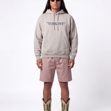 Front of male model wearing grey hoodie with blue "TOURIST" print on the middle chest