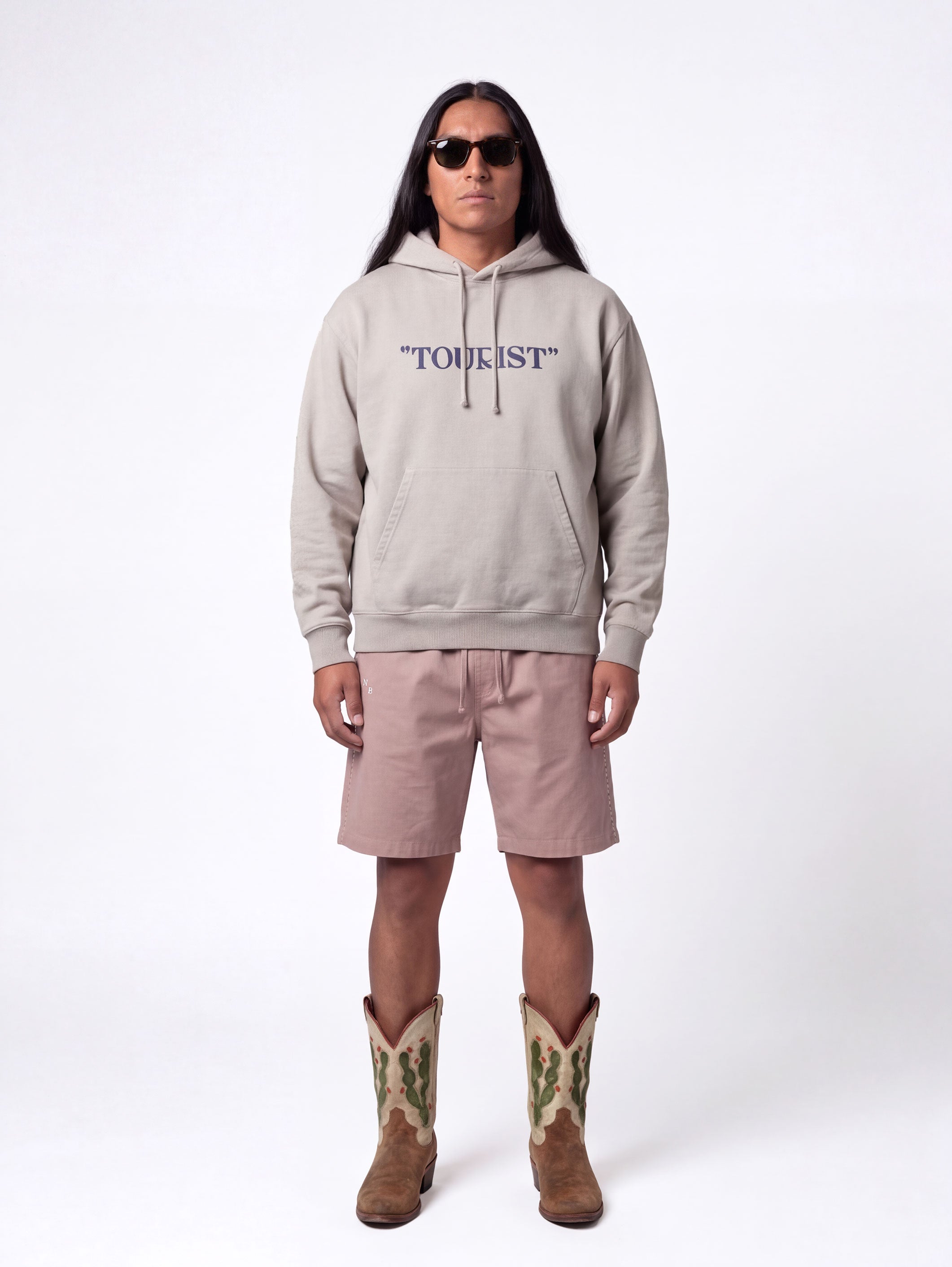 Front of male model wearing grey hoodie with blue "TOURIST" print on the middle chest