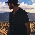 Male model wearing a navy blue short sleeve shirt with white button closure and one chest pocket