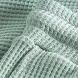 Close up of stitchings and waistband on mint green waffle-patterned mid-length shorts.