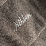 Close up of white embroidered logo on the back of a dark grey short sleeve shirt.