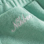 Close up of embroidered logo on grey-green low cut shorts in terry toweling fabric
