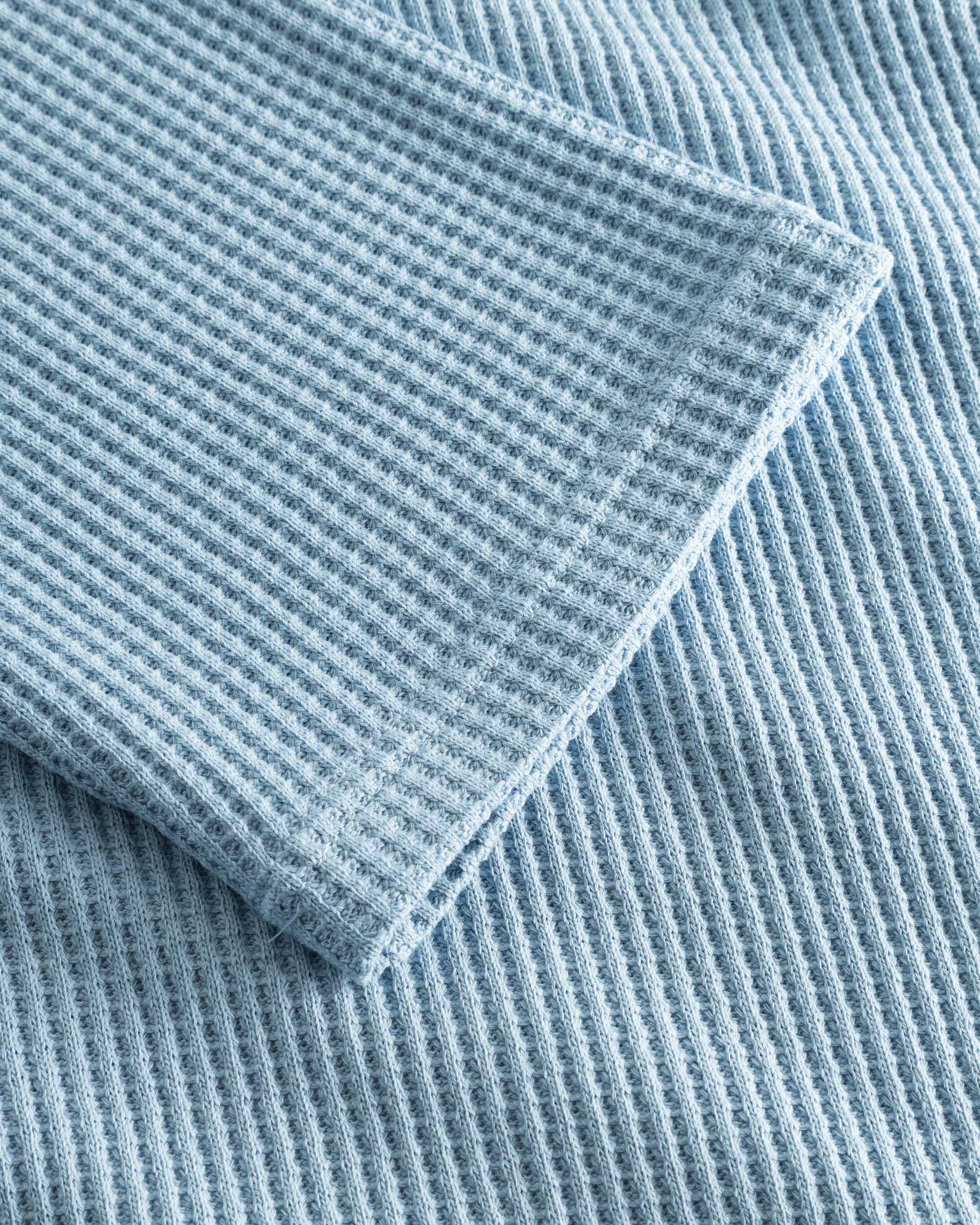Close up on stitchings and sleeve on a sky blue waffle-patterned sweatshirt